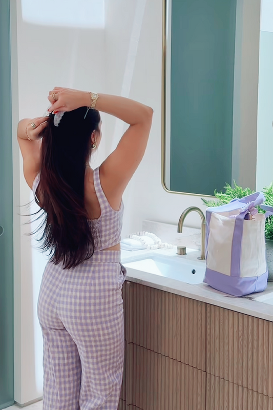 Woman styling her hair in front of a mirror in a bathroom.