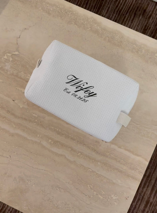 A chic white textured pouch embroidered with ‘Wifey’ and a custom established date. Perfect personalized bridal gift, anniversary keepsake, or wedding day accessory bag.