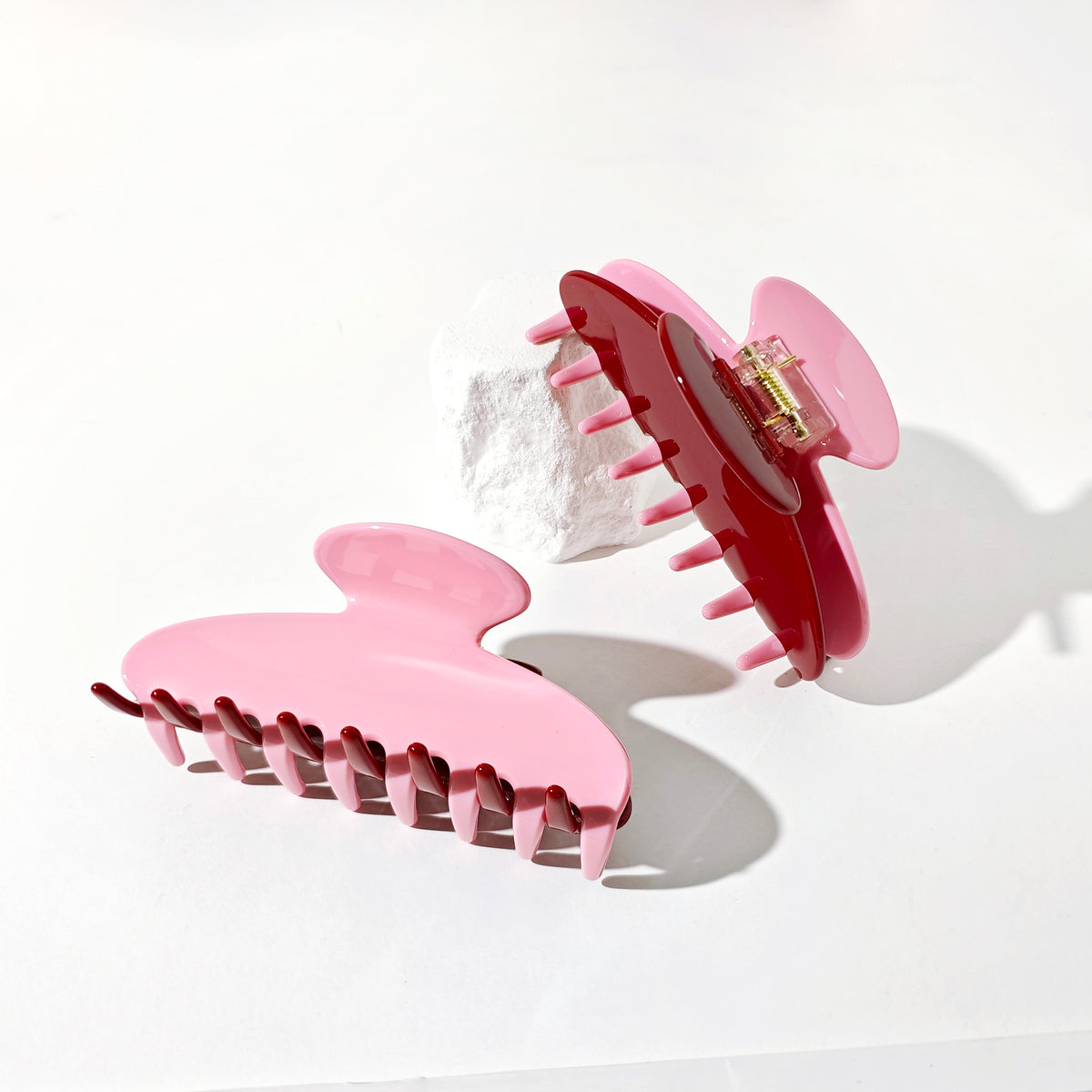 Two hair claw clips in a glossy pink and deep red/burgundy finish, displayed on a clean white background with a small white decorative object.